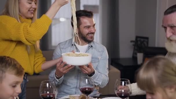 Happy cheerful mother putting spaghetti on grandfathers plate during family dinner — Stock Video