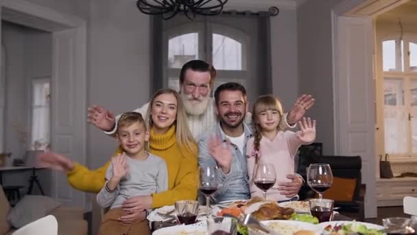 Riendo feliz gente-parientes sentados en la mesa festiva y mirando a la cámara con las manos agitadas — Vídeo de stock