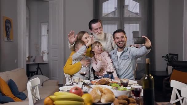 Primer plano de alegre familia agradable que se sienta alrededor de la mesa y hacer selfie — Vídeos de Stock