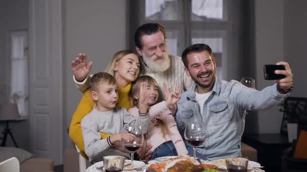 Framsidan av charmiga skrattar familj som sitter vid middagsbordet och gör selfie — Stockvideo