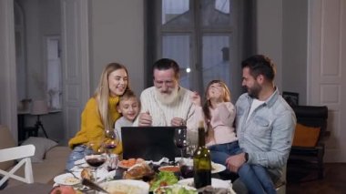 Aile, şenlikli yemek masasındaki bilgisayardaki eğlenceli fotoğrafları incelerken...