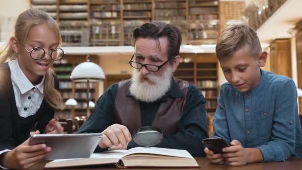 Уважаемый бородатый мужчина 70 лет разочаровывает, потому что 12-летние внуки играют на современных устройствах, а не читают захватывающую книгу — стоковое видео