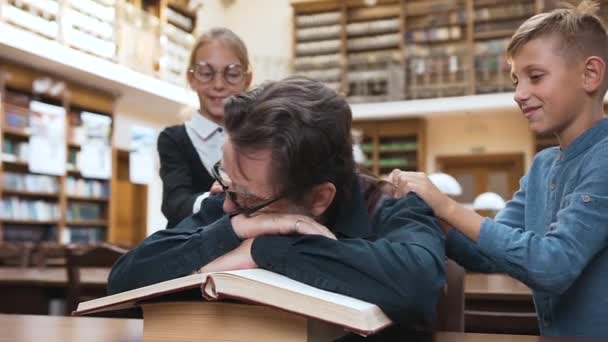 Teenager wecken ihren müden Großvater, der auf Büchern schläft — Stockvideo