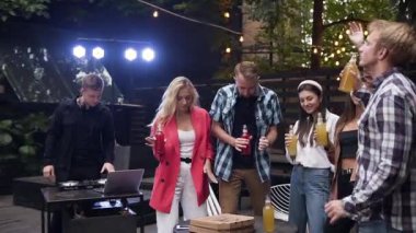 Bir grup arkadaş bira ya da alkol kokteyli içiyor, müzik eşliğinde dans ediyor, sohbet ediyor ve dışarıda akşam partisinde iyi vakit geçiriyorlar.