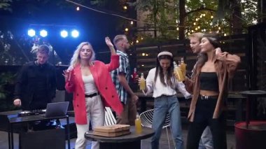 Açık hava partisinde iyi vakit geçirirken Dj 'in müziğiyle dans eden beyaz bir grup genç.