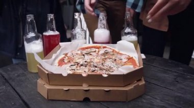 İnsan elleri partideki açık kutudan sıcak İtalyan pizzasından dilimler alıyor. Yemek servisi. Arkadaşlar yemek yerken eğleniyor ve az alkollü içecekler birlikte takılıyor.