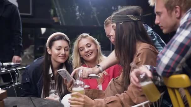 Unga människor som använder app titta på bilder på smartphone till och ha roligt i lusthus på utomhus, de skrattar, skämtar och dricker låg alkohol — Stockvideo