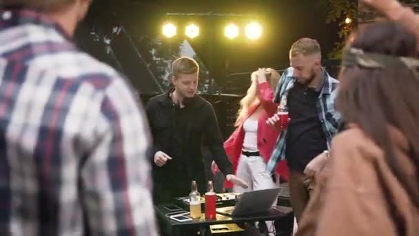 Fête, DJ mixer de la musique avec console de mixage tandis que le groupe de jeunes gens heureux dansent et boivent une boisson faible en alcool en s'amusant sur la célébration. À l'extérieur — Video