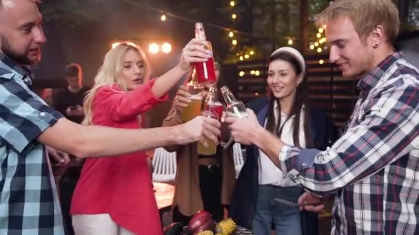 Jovens alegres se divertindo na festa e batendo garrafas com bebidas coloridas durante a reunião de companheiros na casa do jardim — Vídeo de Stock