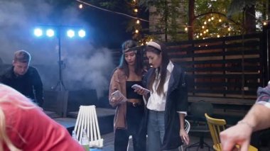 İki kız arkadaş DJ seti yakınlarında konuşuyor ve akıllı telefon kullanıyor. Çekici erkek arkadaş hafta sonları dışarıda sebze pişirirken kız ve erkek arkadaş da masa oyunu oynuyor.