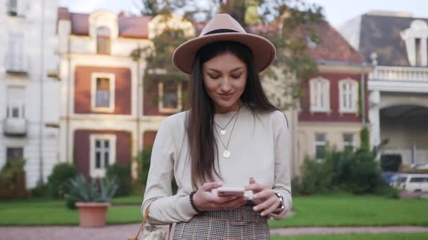 Захватывающая красивая молодая женщина звонит своей подруге, стоя перед богатыми роскошными домами — стоковое видео