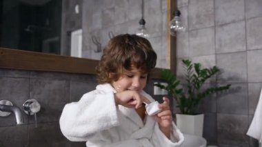 Çekici 5 yaşındaki kahverengi kıvırcık saçlı çocuk banyoda anne kremiyle oynuyor.