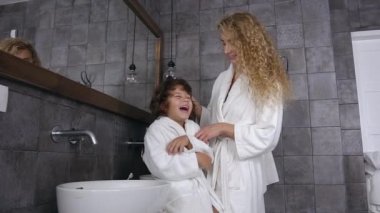 Gecelikli, güzel, sarışın bir kadın fırçalı oğullarıyla banyoda kıvırcık saçları var.