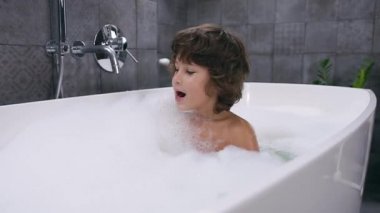 Gülümseyen 5 yaşında, kahverengi saçlı, köpükle banyo yapan hoş bir çocuk.