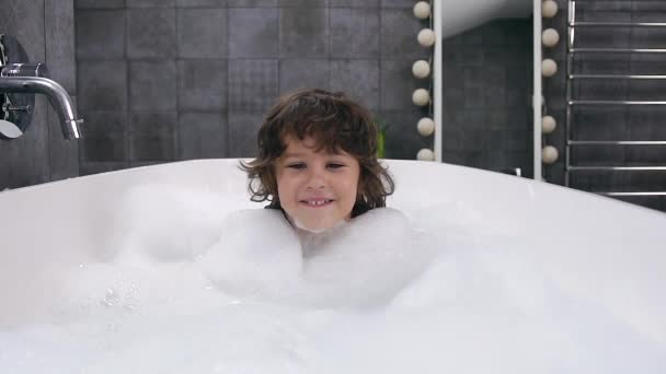 Vista frontal de niño alegre con el pelo castaño que toma un baño con espuma y mirando a la cámara — Vídeo de stock