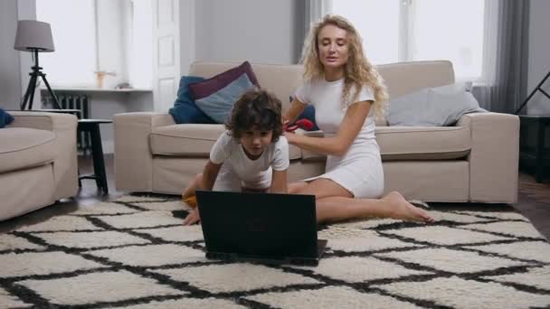 Joyful despreocupado linda mãe e filho sentado no tapete perto do sofá e jogar videogame no computador com joysticks — Vídeo de Stock