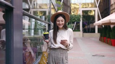 Caddedeki kafenin yanında duran ve cep telefonunu kullanan şık şapkalı hoş, güler yüzlü genç bayanın ağır çekimleri.