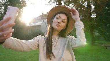 Yeşil bahçede güzel selfie çeken şık şapkalı, neşeli, güler yüzlü bir kadının çekici portresi.