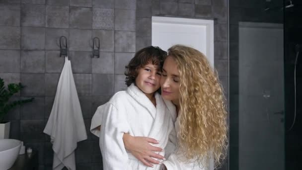 Attractive portrait of smiling happy good-looking mother and son in dressing gowns which looking at camera in the bathroom — Stock Video