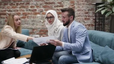 Modern ofisteki yumuşak koltuklarda oturan, iş projesinde birlikte çalışan, yetenekli, bilge, farklı etnik kökenden insanların çekici bir resmi.