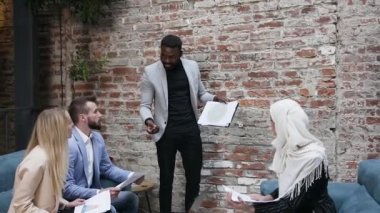Şirin Müslüman iş kadını, erkek ve kadın iş ortaklarıyla birlikte ofis koltuklarında oturuyor ve sakallı Afro-Amerikan iş adamlarının raporunu çizelgeyle açıklıyor.