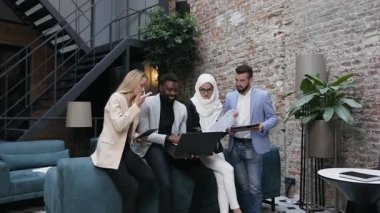 Modern ofisteki kanepeye yaslanıp ortak projeyi tartışan çok ırklı genç iş adamları ve iş kadınlarının çekici portresi.
