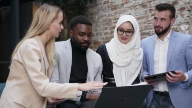 Bilgisayar ekranından izleyen ve yeni moda ofiste ortak çalışmaları hakkında konuşan dört çok ırklı iş adamının ön görüntüsü.