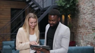 Çekici sarışın kadın işçi ve sakallı Afro-Amerikan iş adamı i-pad kullanıyor ve modern ofiste konuşuyor.