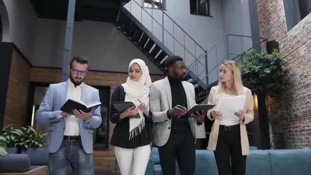 Druk 35 's goed uitziende multiraciale zakenmensen gaan door de kantoorruimte en houden in hun handen documenten, boek en i-pad — Stockvideo