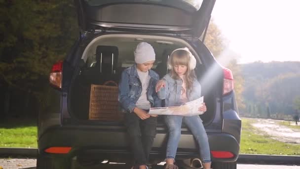 Güzel genç çocuklar bagajda oturur ve aile gezilerinden önce yol haritasına bakarlar. — Stok video