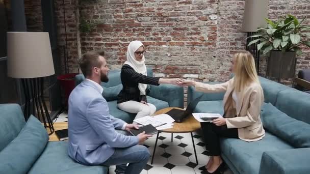 Успешная мусульманская деловая женщина пожимает руку двум кавказским клиентам во время важной сделки в офисе — стоковое видео