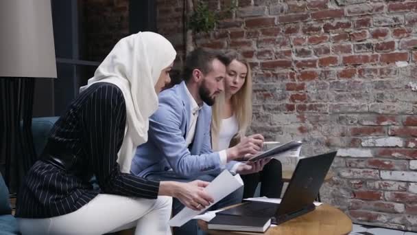 International business people collaborating together during the meeting sitting in specially office place while using documents and laptop and conversing about their success business project — ストック動画