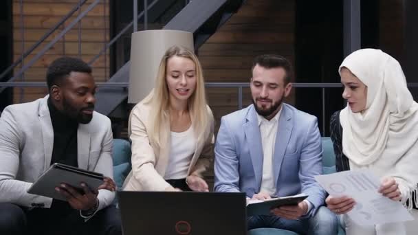 Vue de face de quatre jeunes partenaires commerciaux internationaux qui se rencontrent et se consultent sur leur projet d'entreprise commune sur le lieu de travail au bureau — Video