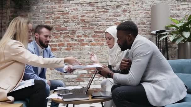 Jovem equipe de negócios internacional de quatro pessoas de sucesso discutir um novo projeto ter papel de trabalho com enquanto sentado em torno da mesa no escritório — Vídeo de Stock