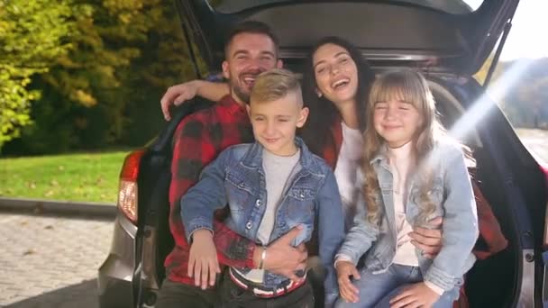 Gros plan de belle famille branchée gaie qui s'assoit dans le coffre et pose sur la caméra avec des sourires sincères — Video