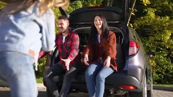 Vista lateral de la encantadora familia joven feliz que se divierten juntos mientras están sentados en el maletero — Vídeos de Stock