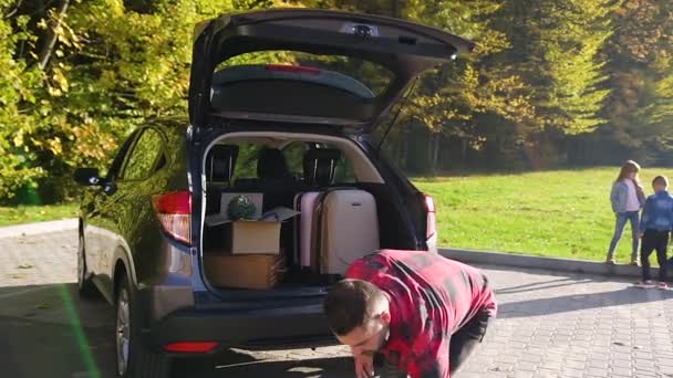 Attractive young bearded man unloading from the trunk green plants,boxes and suitcases during moving to the new home — Stock Video