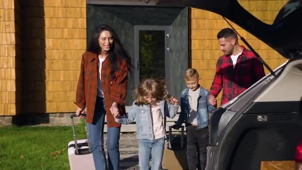 Přední pohled na dobře vypadající usmívající se rodinu, která nakládá svá zavazadla do kufru před společnou cestou autem — Stock video