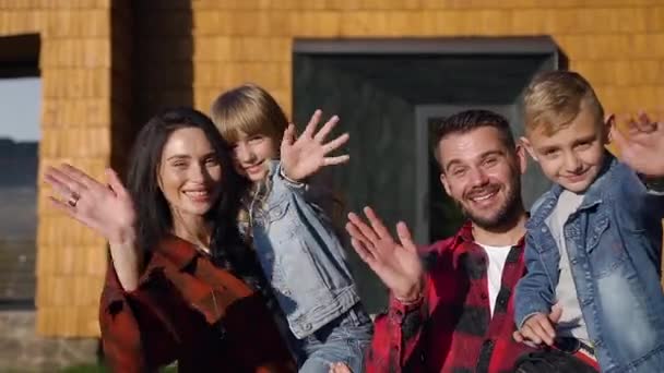 Привабливий портрет щасливої радісної сучасної сім'ї, яка позує на камеру біля красивого будинку і махає руками — стокове відео