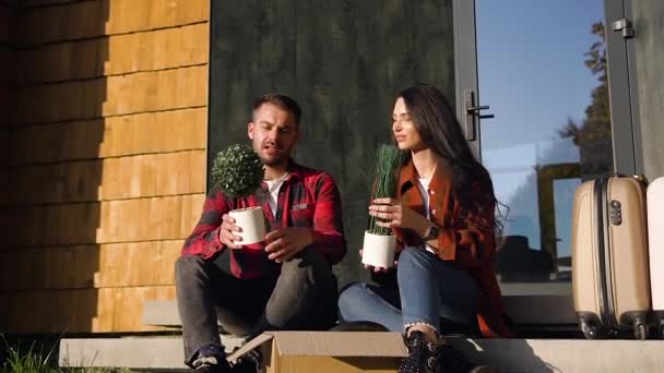 Bonita pareja feliz de 35 años sentados en las escaleras de las casas y hablando entre sí durante su mudanza a un nuevo hogar — Vídeo de stock