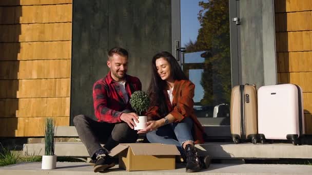 Привлекательный портрет прекрасного современного мужчины и женщины, которые сидят на ступеньках, держа в руках зеленый цветок и глядя в сторону — стоковое видео