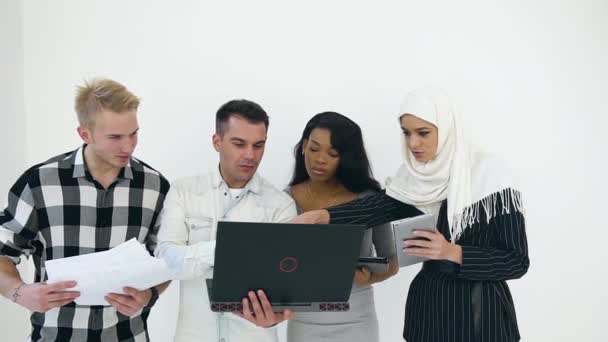 Vue de face de jeunes gestionnaires de bureau multiraciaux agréables qui parlent entre eux tout en travaillant ensemble près de mur blanc — Video