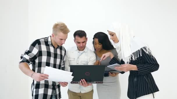 Ernsthafte multiethnische angenehme Büroangestellte, die am Computer sitzen und Projektdetails in der Nähe weißer Wände besprechen — Stockvideo