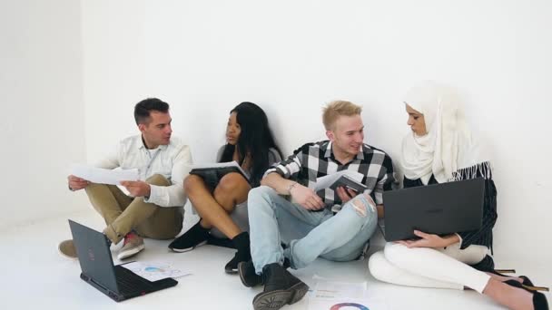 Joyful experiente jovens multiétnicos homens e mulheres sentados no chão do escritório e discutindo os detalhes de seu projeto conjunto — Vídeo de Stock