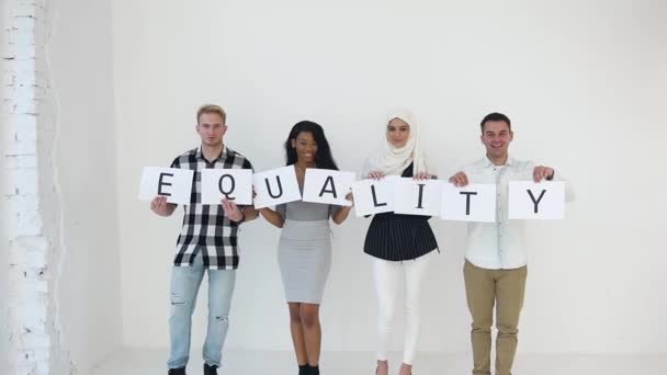 Sonrientes jóvenes de raza mixta moderna que llevan la inscripción "Igualdad", de pie sobre el fondo blanco — Vídeo de stock