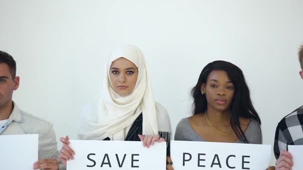 Привлекательная фотография четырех серьезных многонациональных молодых людей, которые позируют на камеру с плакатами с надписью "Свободная любовь. Мир не война.Сохранить планета.Нет расизма " — стоковое видео