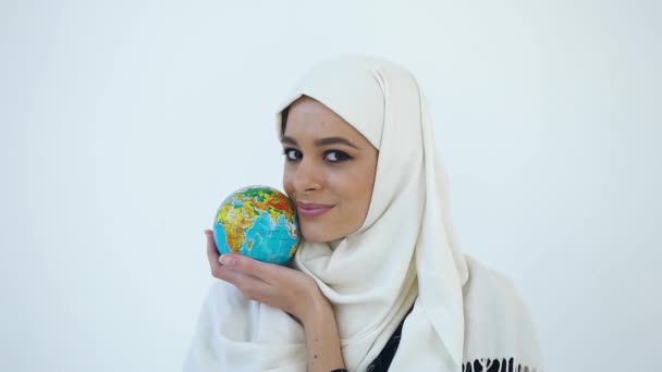 Belo retrato da jovem mulher muçulmana sorridente feliz em hijab que olhando para a câmera e segurando perto de seu rosto pequeno globo — Vídeo de Stock