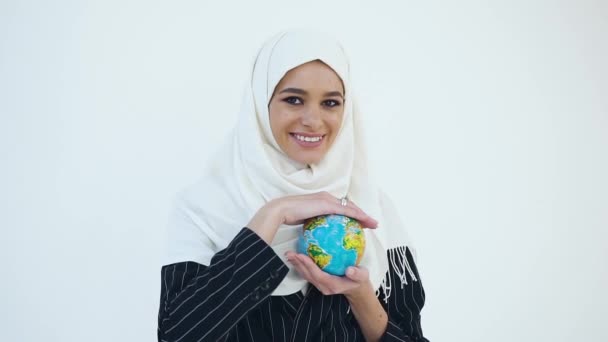 Magnifincent jonge vrolijke moslim vrouw in hijab staan op de witte achtergrond en poseren op camera met kleine wereldbol in haar handen — Stockvideo