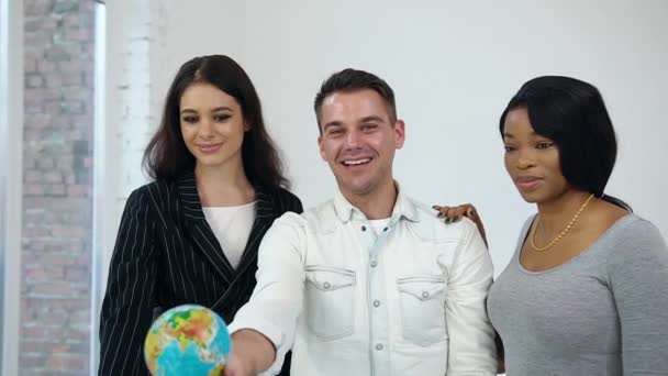 Adorable modern multiethnic youth in beautiful clothes posing on white background and putting their hands on little globe,symbolizing united nations — 비디오