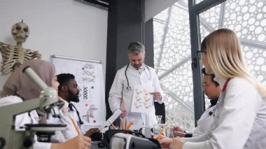 Hastane ofisinde oturan ve beyaz saçlı erkek doktorlarının raporunu dinleyen yüksek yetenekli melez ırk doktorlarının çekici bir resmi.
